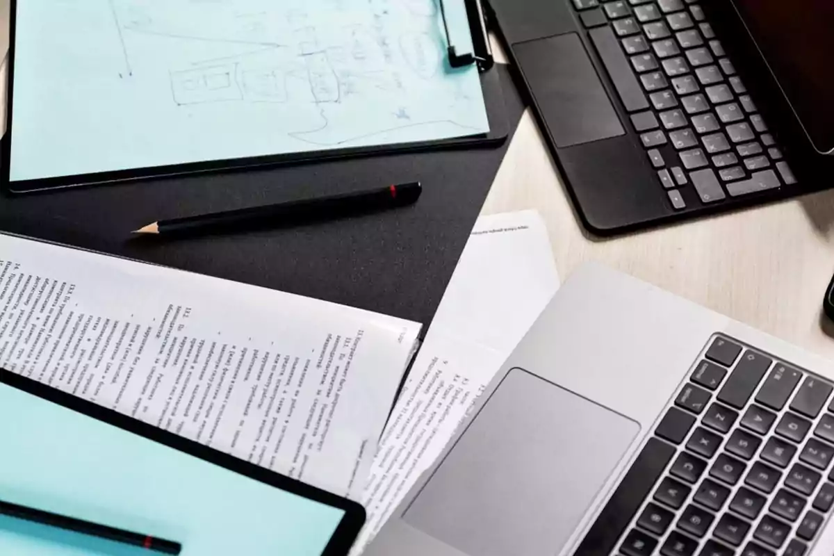 Un escritorio con una laptop, documentos, un lápiz y un cuaderno con notas.