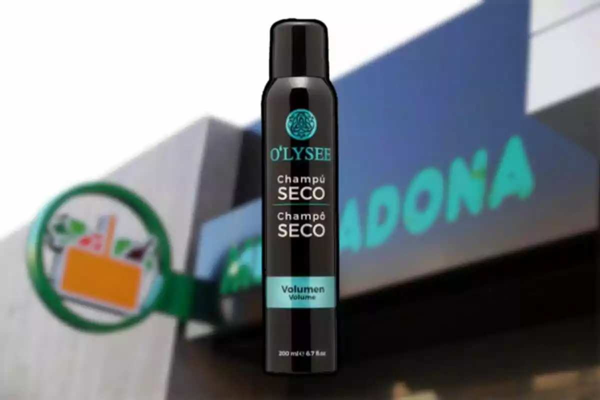 Una botella de champú seco O'LYSEE frente a un cartel de supermercado.