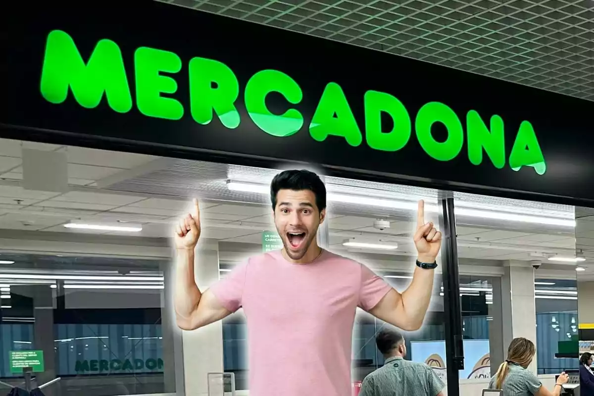 Un hombre con camiseta rosa señala con ambas manos hacia arriba, donde se encuentra el letrero de una tienda que dice "Mercadona".