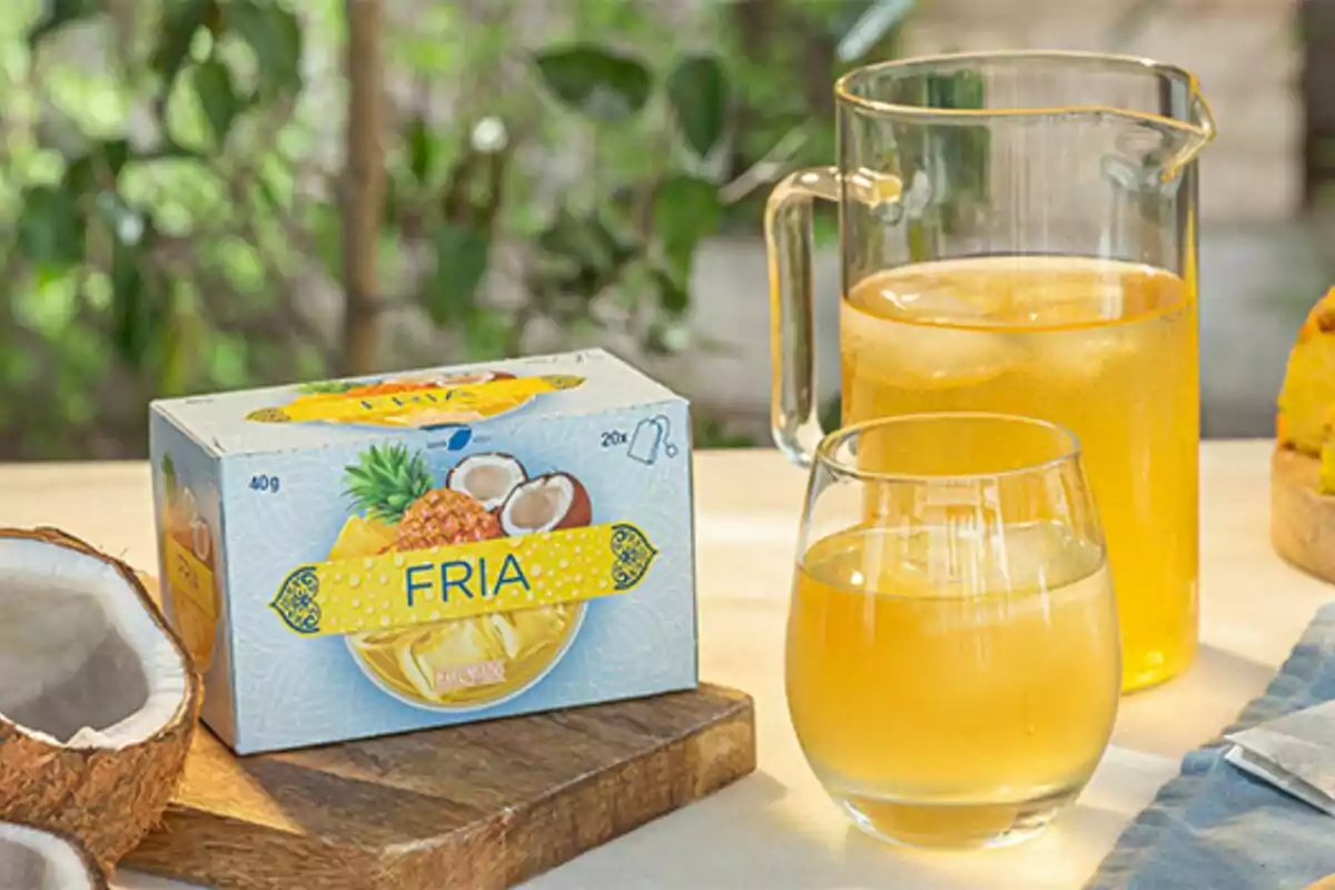 Caja de bebida en polvo sabor piña y coco junto a una jarra y un vaso con la bebida preparada sobre una mesa. Caja de bebida en polvo sabor piña y coco junto a una jarra y un vaso con la bebida preparada sobre una mesa.