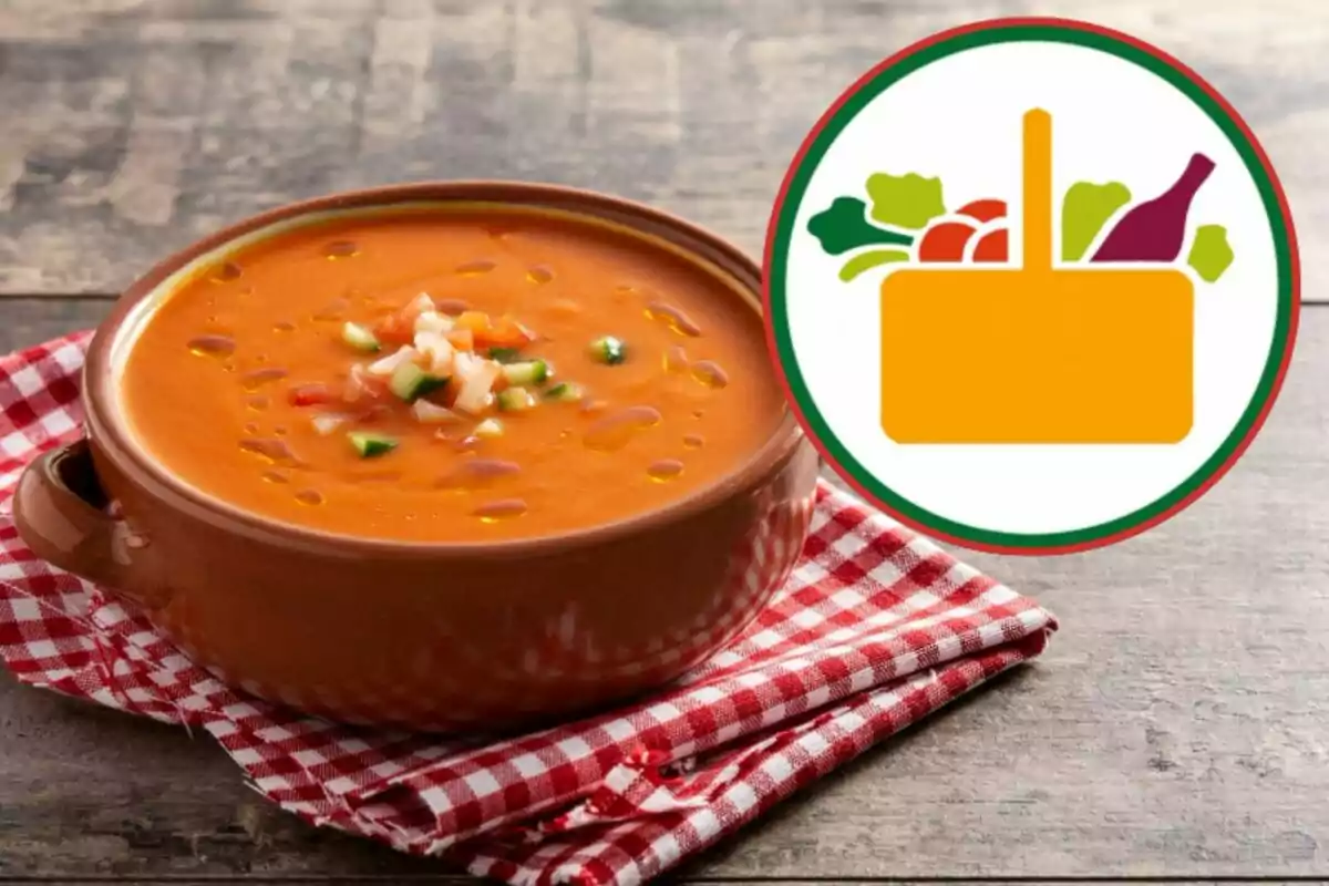 Sopa de tomate en un cuenco de barro sobre un mantel a cuadros rojos y blancos con un icono de alimentos al lado.