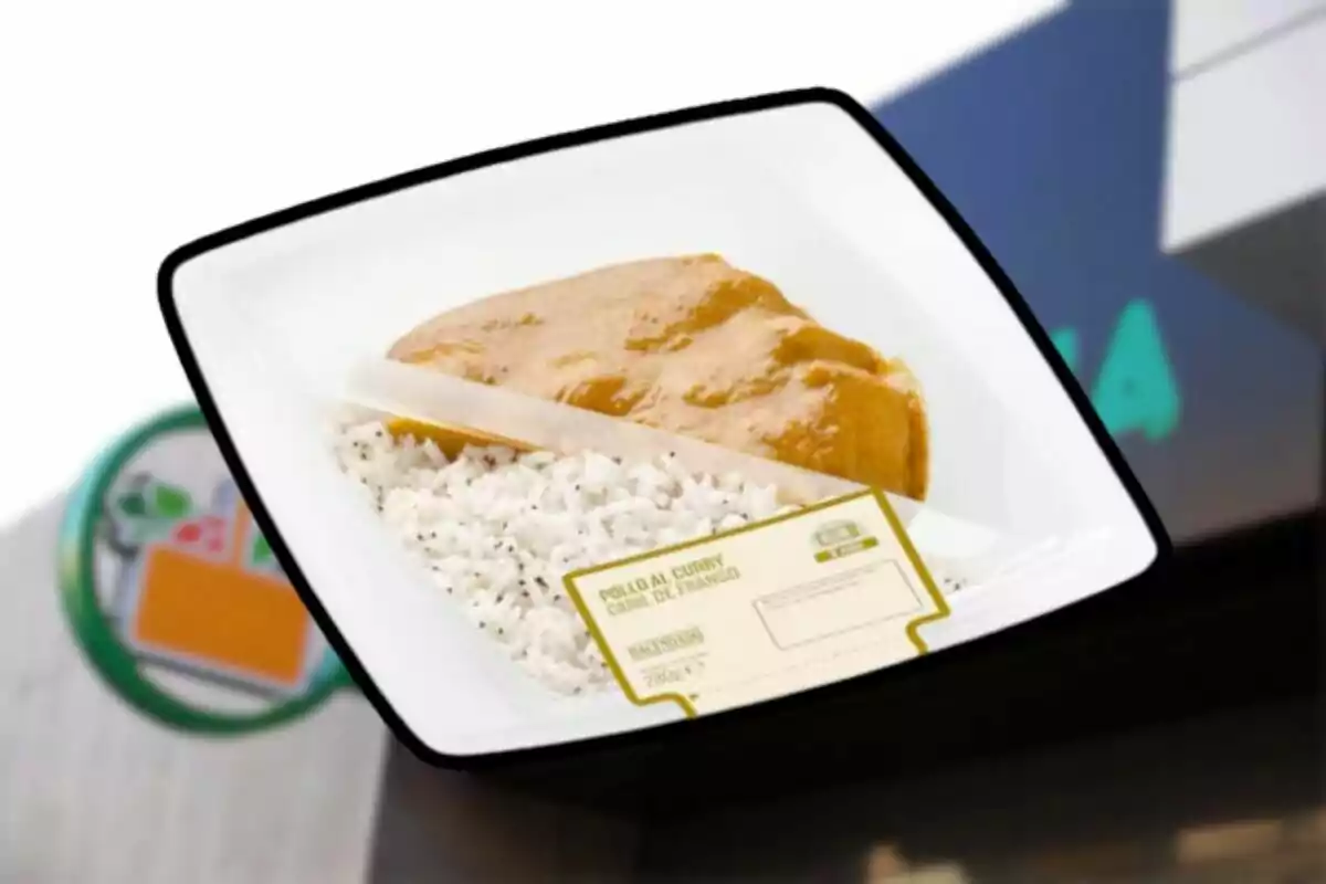 Un plato de pollo al curry con arroz en un envase de plástico frente a un fondo borroso. Un plato de pollo al curry con arroz en un envase de plástico frente a un fondo borroso.