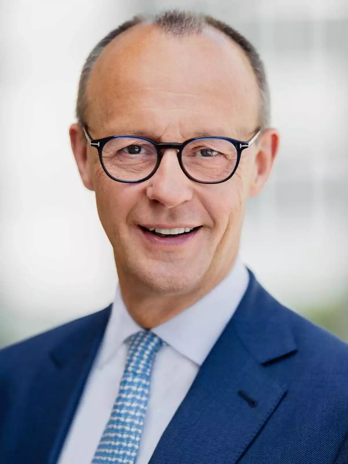 Man with glasses and a blue suit smiling.