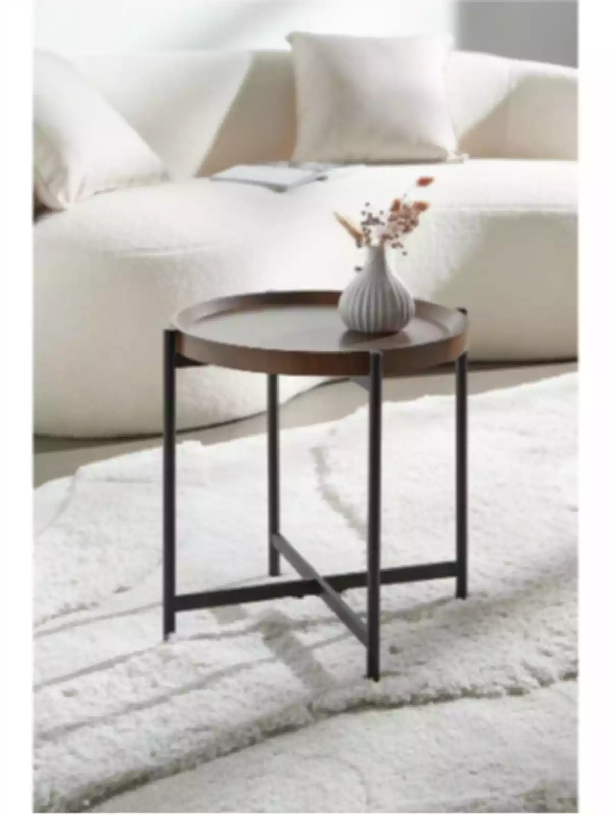 Mesa auxiliar redonda de madera con patas metálicas negras, decorada con un florero pequeño, frente a un sofá blanco sobre una alfombra clara Mesa auxiliar redonda de madera con patas metálicas negras, decorada con un florero pequeño, frente a un sofá blanco sobre una alfombra clara