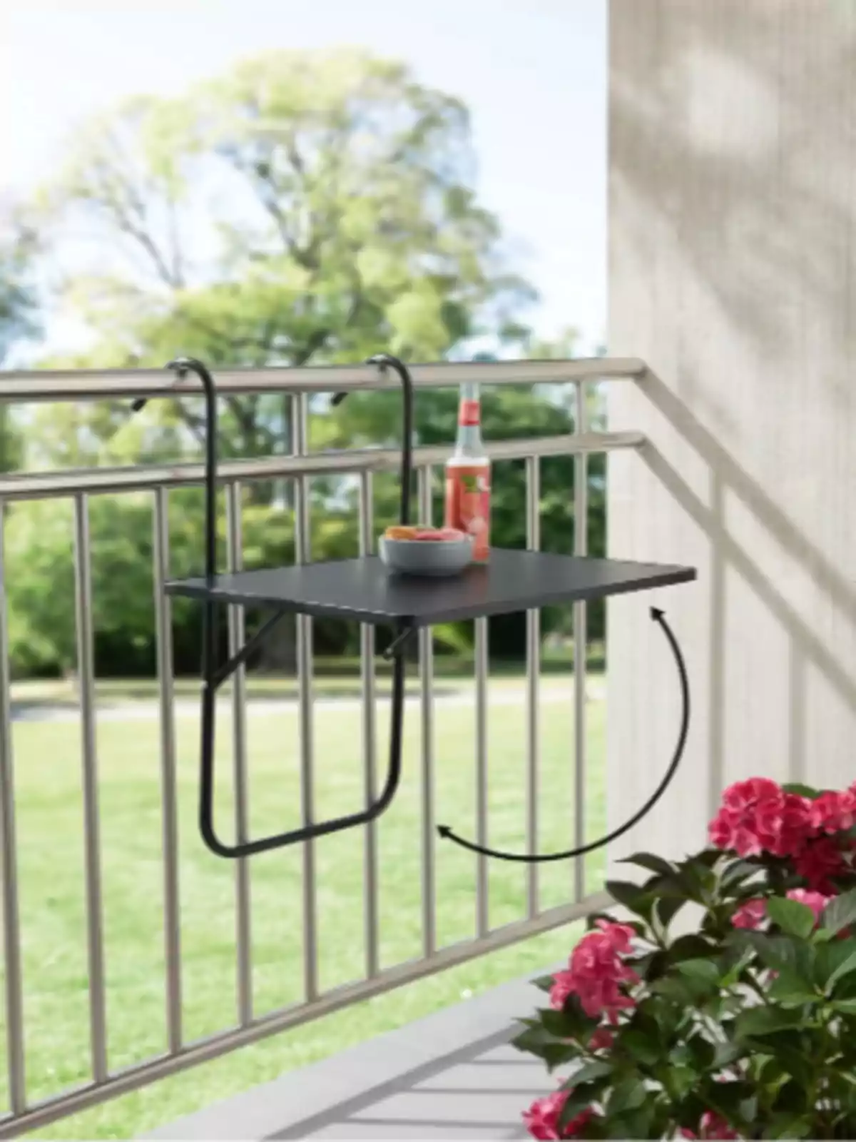 Mesa plegable negra colgada en una barandilla de balcón con una bebida y un tazón, rodeada de plantas y un paisaje verde al fondo. Mesa plegable negra colgada en una barandilla de balcón con una bebida y un tazón, rodeada de plantas y un paisaje verde al fondo.