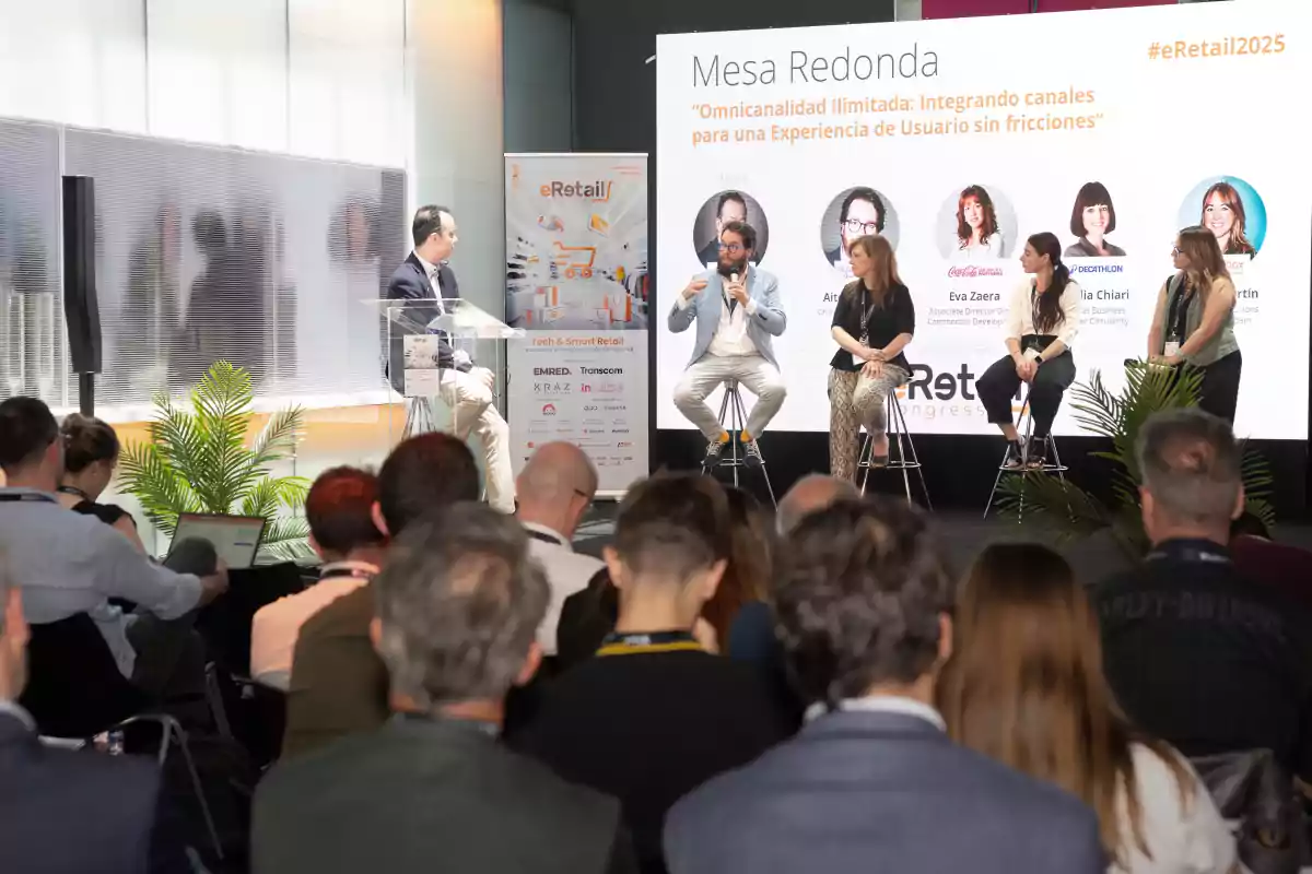 Un grupo de personas participa en una mesa redonda sobre experiencia de usuario en un evento de eRetail mientras el público escucha atentamente
