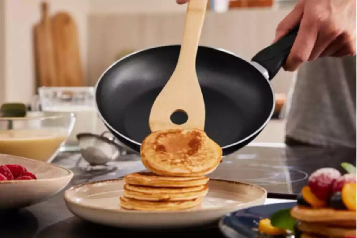 Persona cocinando panqueques en una sartén, apilándolos en un plato en una cocina. Persona cocinando panqueques en una sartén, apilándolos en un plato en una cocina.