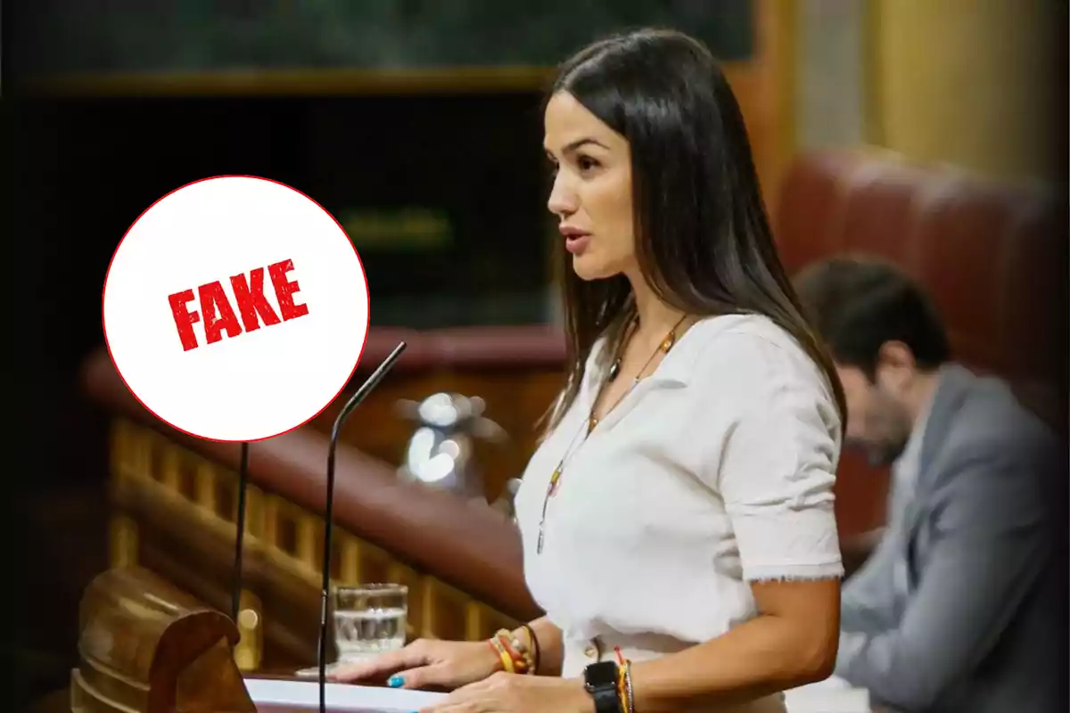 Woman speaking at a podium with a circle containing the word "FAKE" in red.