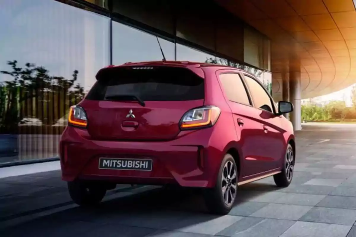 Un automóvil Mitsubishi rojo estacionado frente a un edificio con paredes de vidrio y un techo moderno.