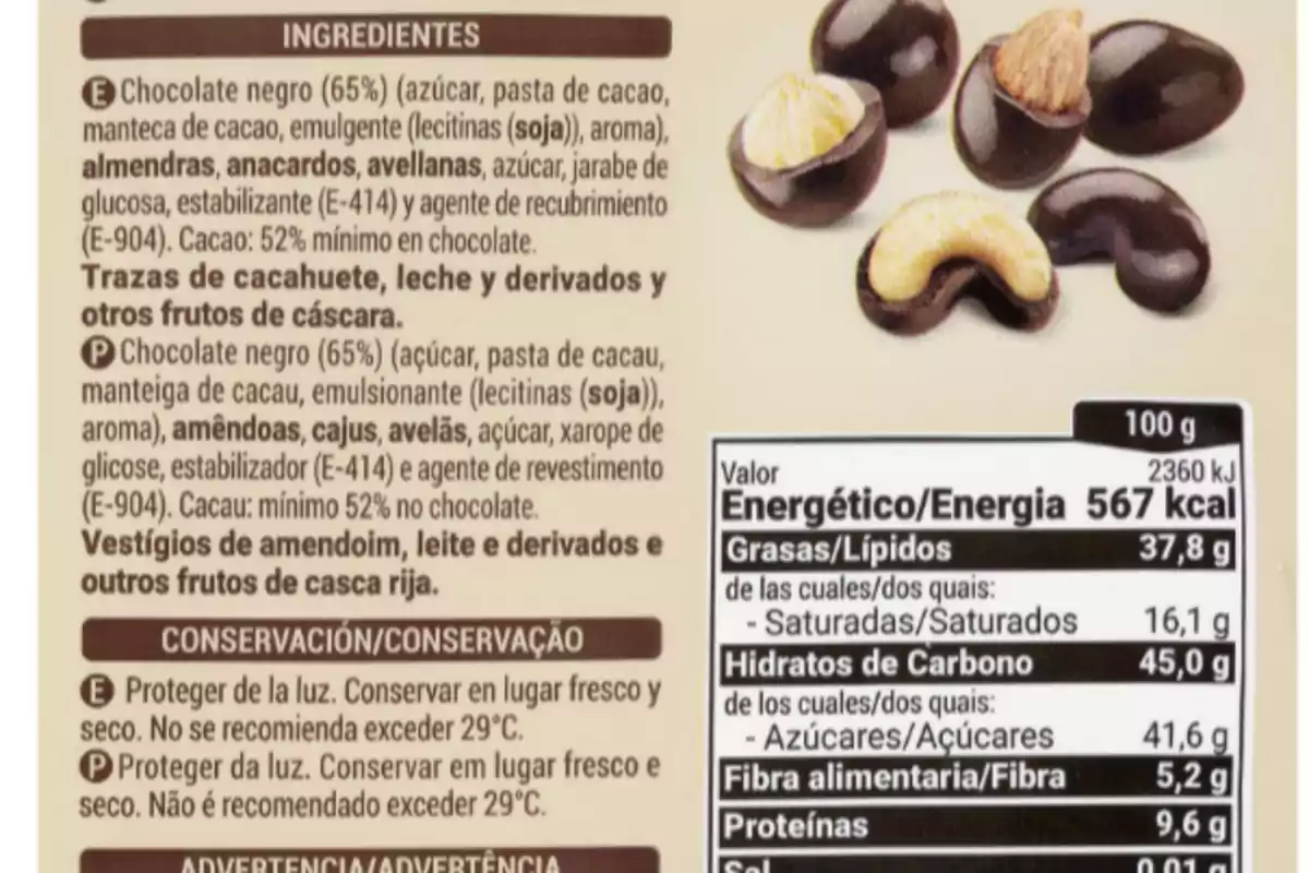 La imagen muestra una etiqueta de ingredientes y valores nutricionales de un producto de chocolate negro con frutos secos, incluyendo almendras, anacardos y avellanas, con advertencias sobre posibles trazas de cacahuete, leche y otros frutos de cáscara, además de instrucciones de conservación y advertencias en español y portugués. La imagen muestra una etiqueta de ingredientes y valores nutricionales de un producto de chocolate negro con frutos secos, incluyendo almendras, anacardos y avellanas, con advertencias sobre posibles trazas de cacahuete, leche y otros frutos de cáscara, además de instrucciones de conservación y advertencias en español y portugués.