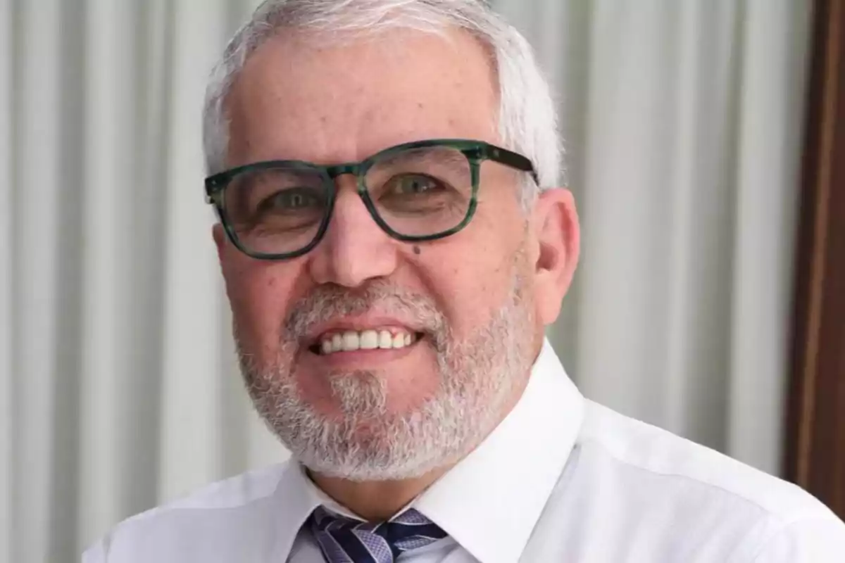 Un hombre con barba y gafas sonríe mientras lleva una camisa blanca y corbata. Un hombre con barba y gafas sonríe mientras lleva una camisa blanca y corbata.