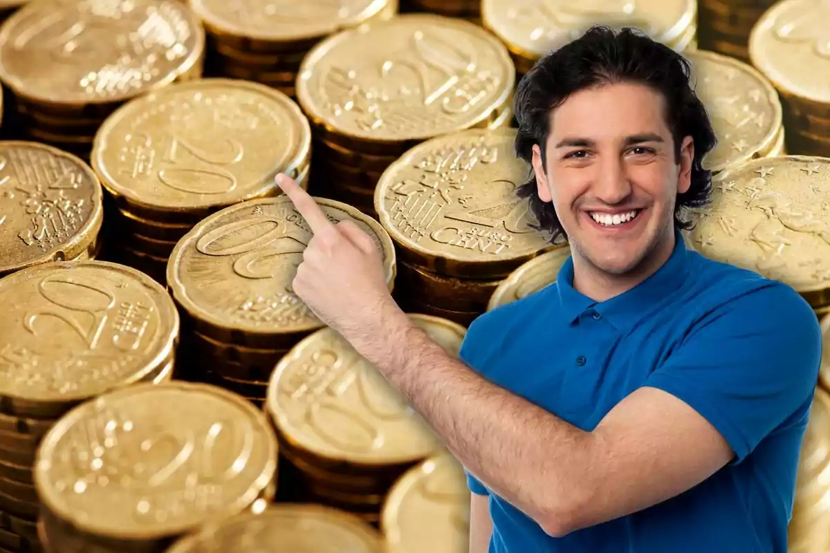 Un hombre sonriente con camisa azul señala hacia una pila de monedas de 20 céntimos de euro.