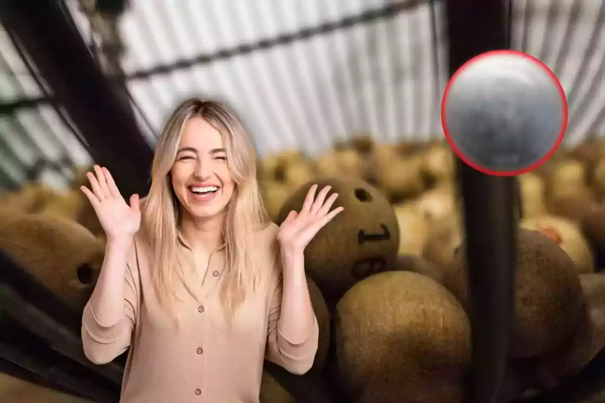 Una mujer sonriente con las manos levantadas frente a un bombo de lotería lleno de bolas numeradas.