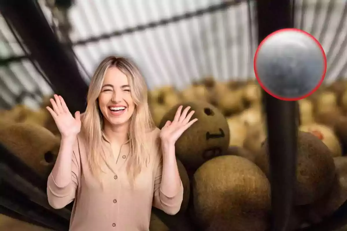 Una mujer sonriente con las manos levantadas frente a un bombo lleno de bolas numeradas.