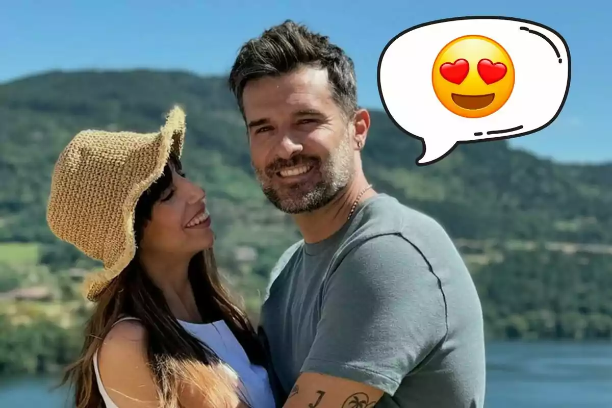 Almudena Cid y Gerardo Berodia sonrientes se abrazan al aire libre con un paisaje montañoso de fondo y un emoji de cara con corazones en los ojos en un globo de diálogo.