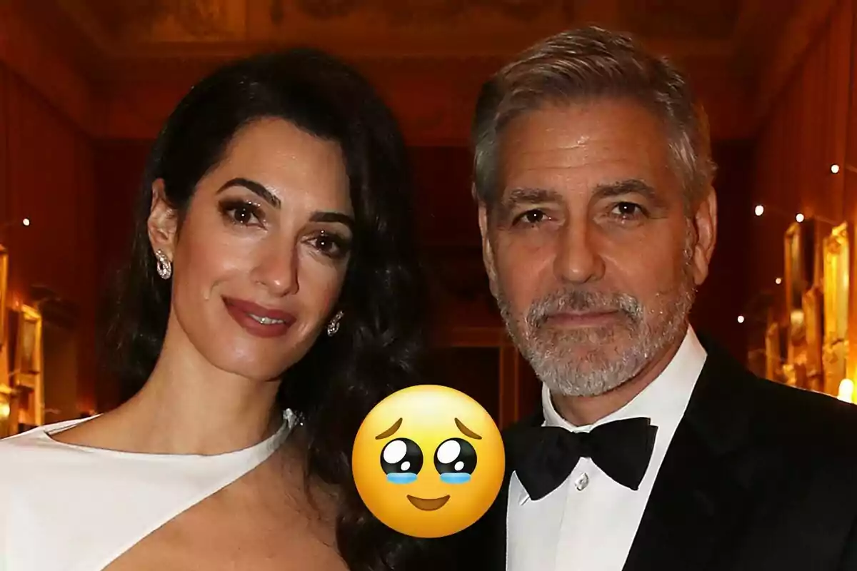 Amal y George Clooney elegantemente vestida en un evento con un emoji emocionado superpuesto.