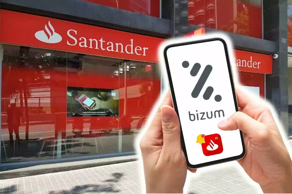 Una persona sostiene un teléfono móvil con el logo de Bizum frente a una sucursal del banco Santander.