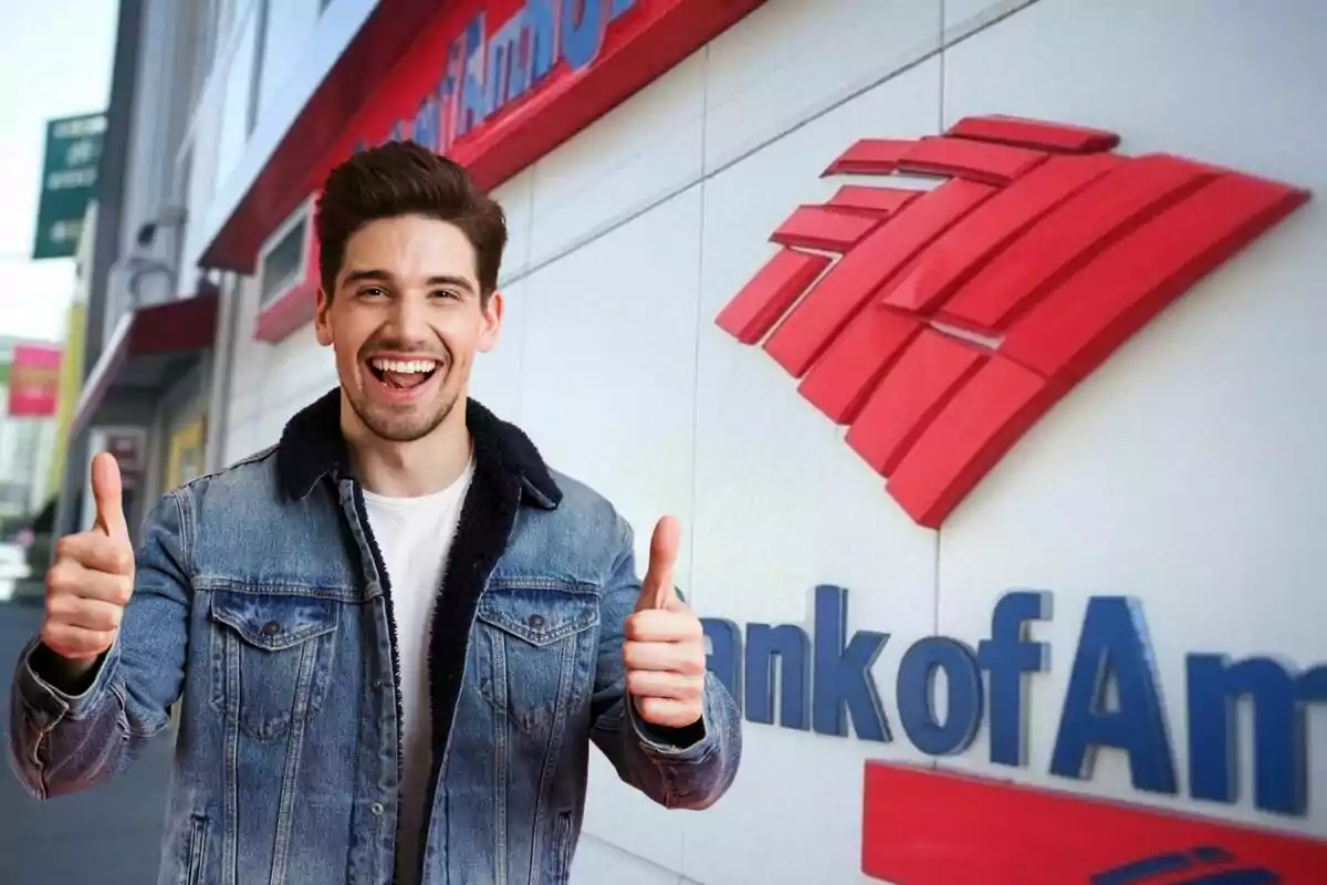 A smiling man in a denim jacket gives a thumbs-up in front of a building with a bank logo.