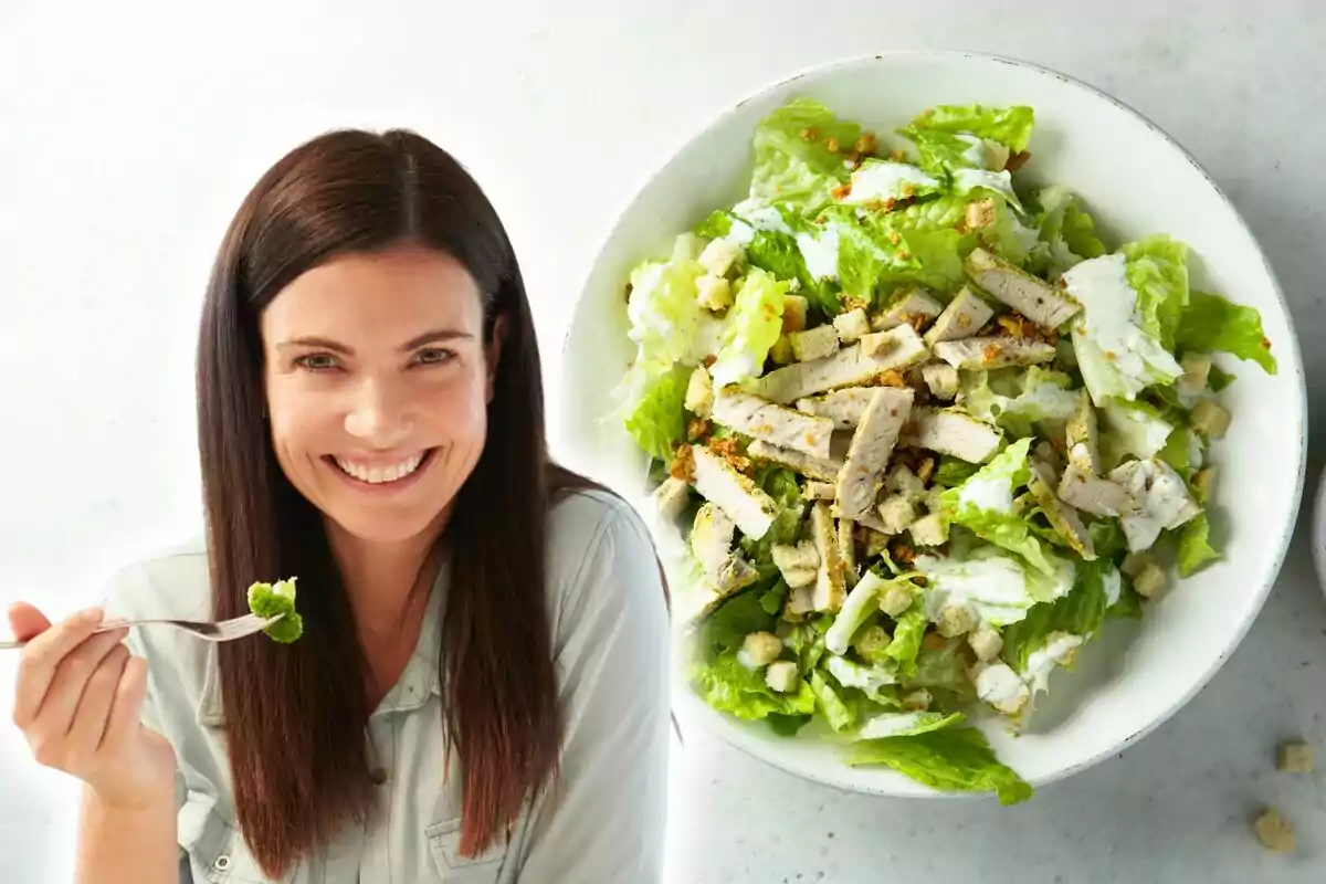 Una persona sonriendo mientras sostiene un tenedor con ensalada junto a un plato grande de ensalada César con pollo. Una persona sonriendo mientras sostiene un tenedor con ensalada junto a un plato grande de ensalada César con pollo.