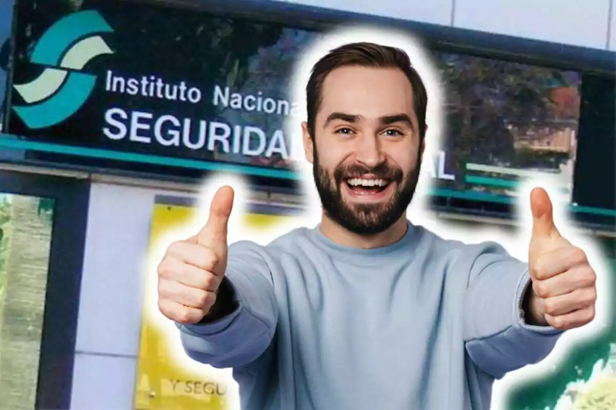 Un hombre sonriente con barba y bigote, vestido con un suéter azul claro, muestra ambos pulgares hacia arriba frente a un edificio del Instituto Nacional de Seguridad Social.