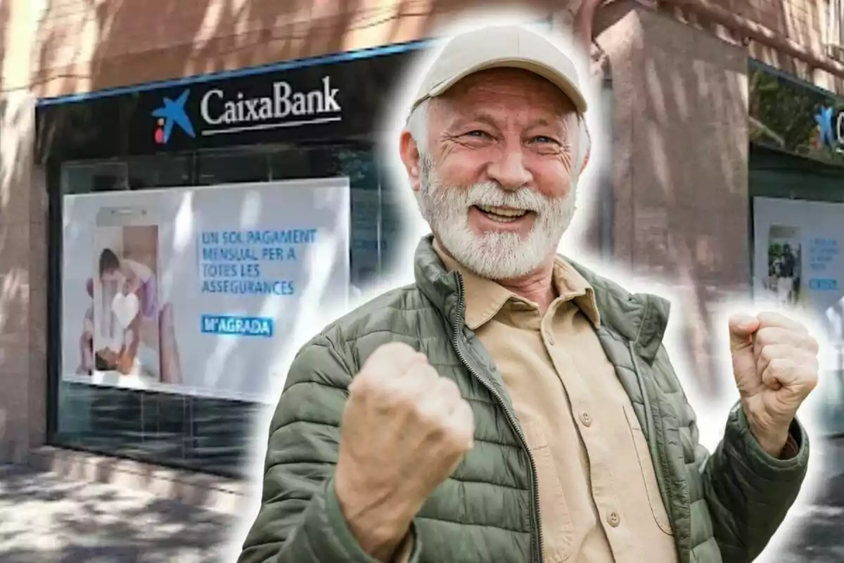 Un hombre mayor con barba blanca y gorra sonríe y levanta los puños en señal de victoria frente a una sucursal de CaixaBank.