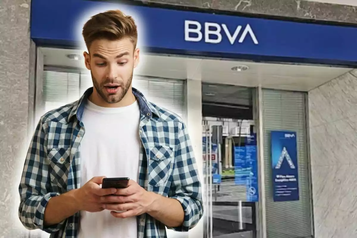 Un hombre sorprendido mirando su teléfono frente a una sucursal de BBVA.