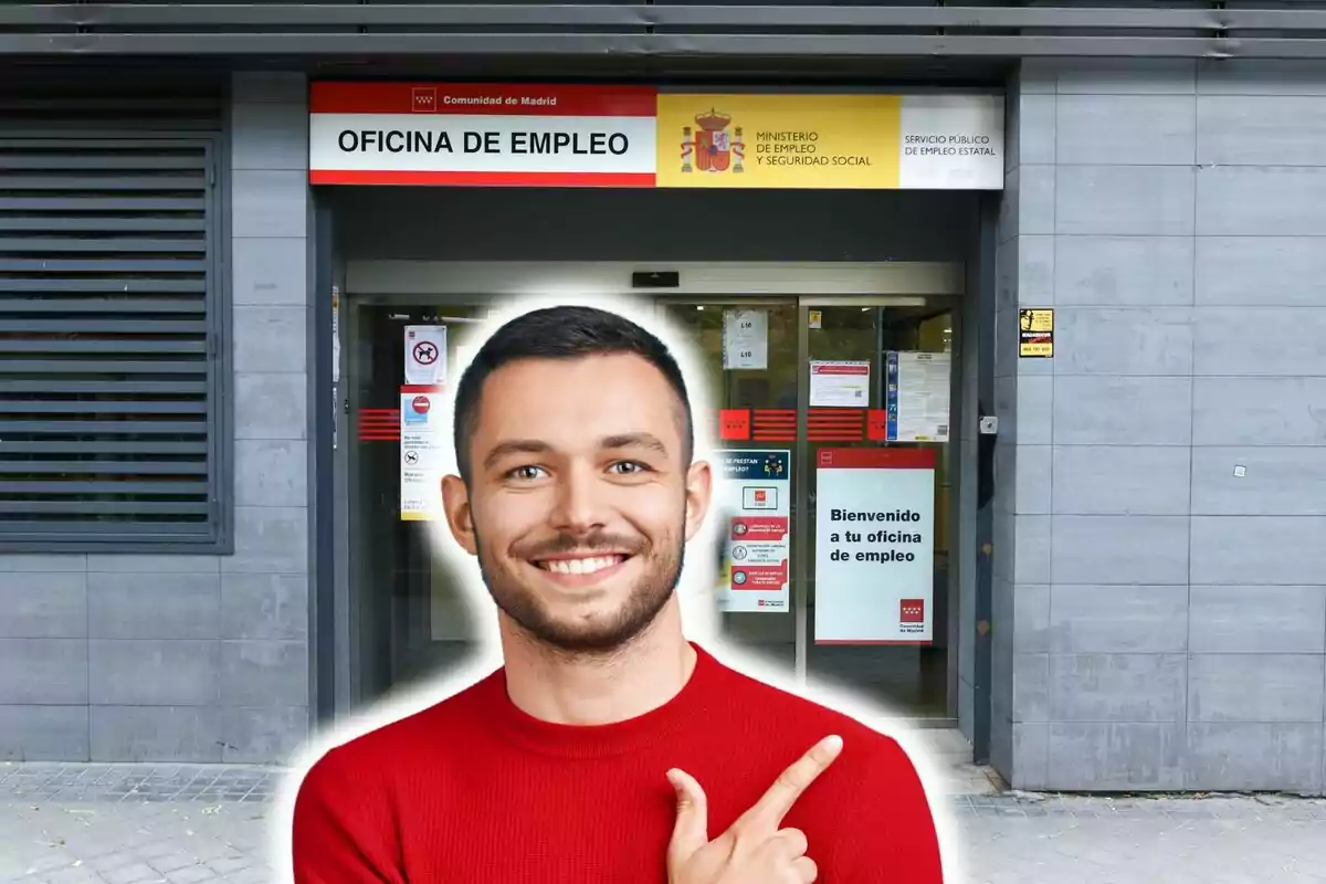 Un hombre sonriente con un suéter rojo señala con el dedo hacia la entrada de una oficina de empleo en Madrid.