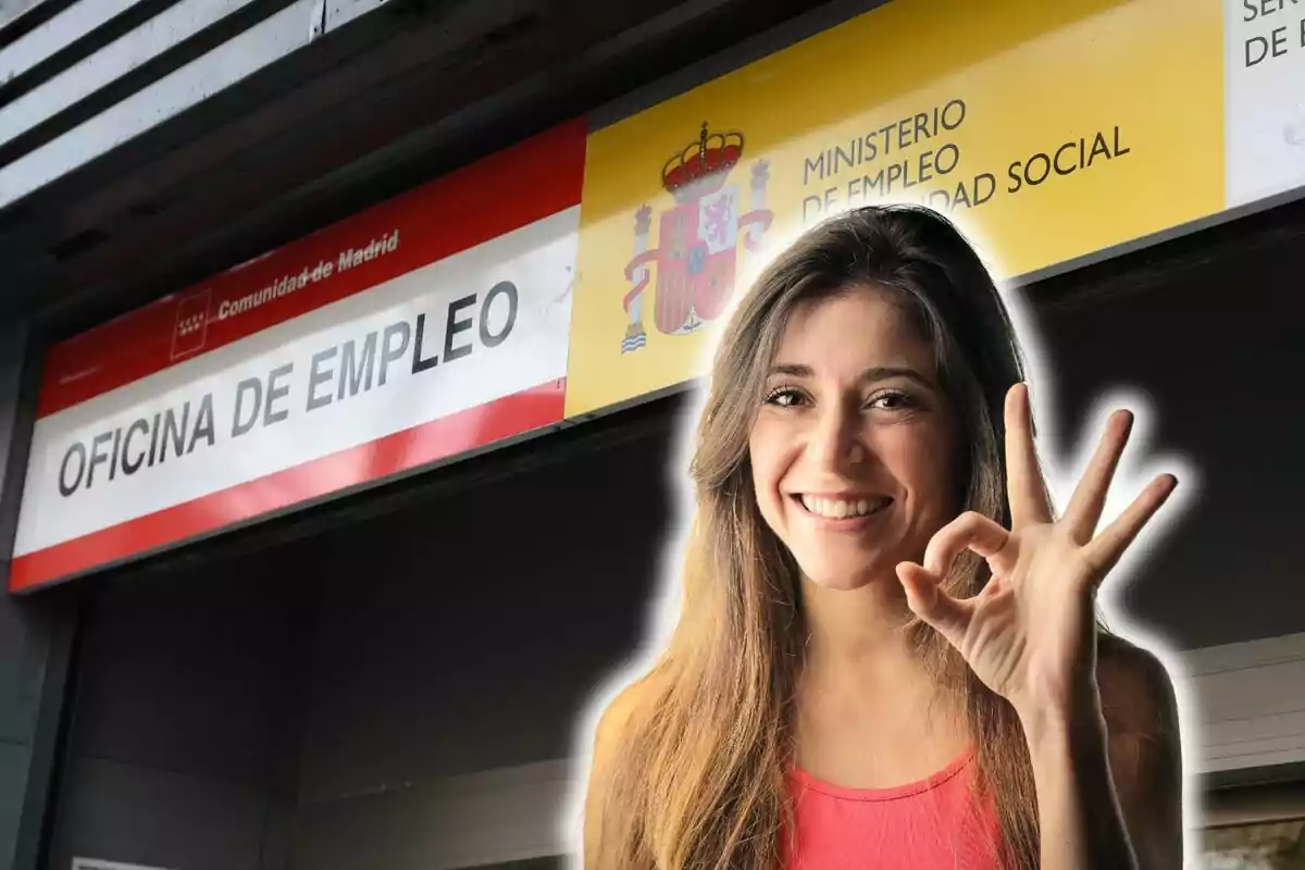 Mujer sonriendo y haciendo un gesto de "ok" frente a una oficina de empleo en Madrid.