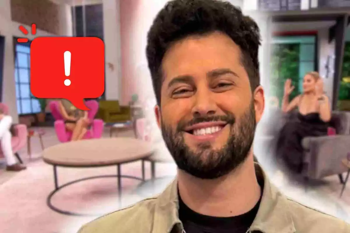 Javier de Hoyos sonriente en primer plano con fondo de sala de estar y personas sentadas en 'D Corazón', una burbuja roja con signo de exclamación cubre parte de la imagen