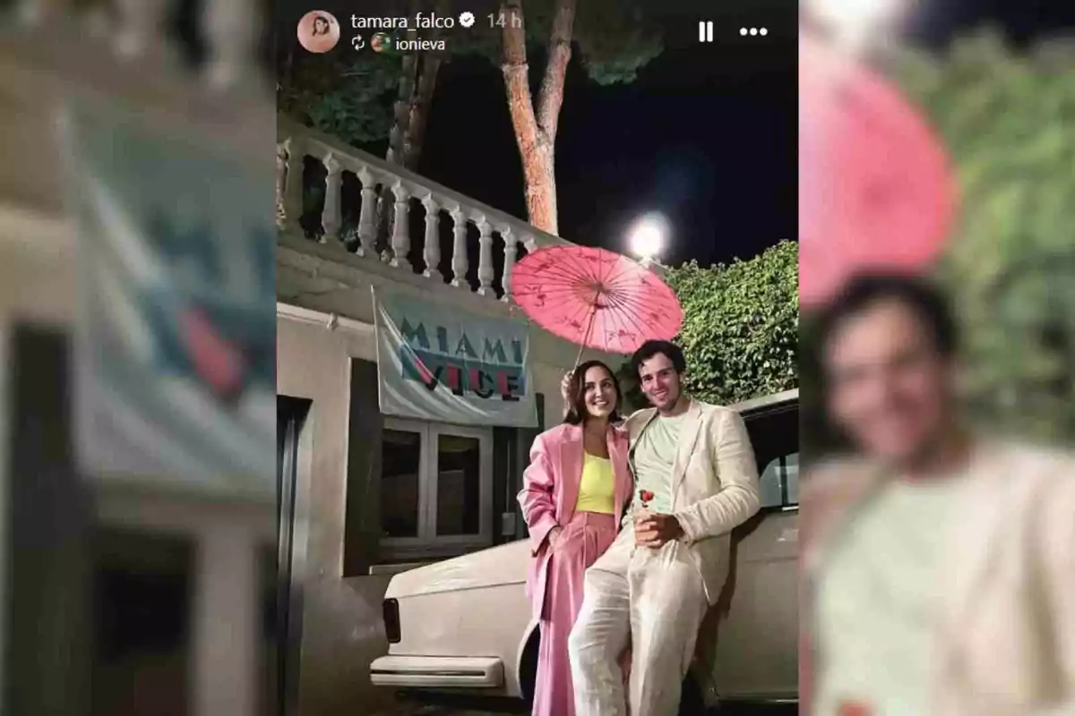 Tamara Falcó e Íñigo Onieva vestidos con ropa elegante de colores claros posando sonriente junto a un coche blanco, ella sostiene un paraguas rosa y detrás hay una pancarta que dice Miami Vice Tamara Falcó e Íñigo Onieva vestidos con ropa elegante de colores claros posando sonriente junto a un coche blanco, ella sostiene un paraguas rosa y detrás hay una pancarta que dice Miami Vice