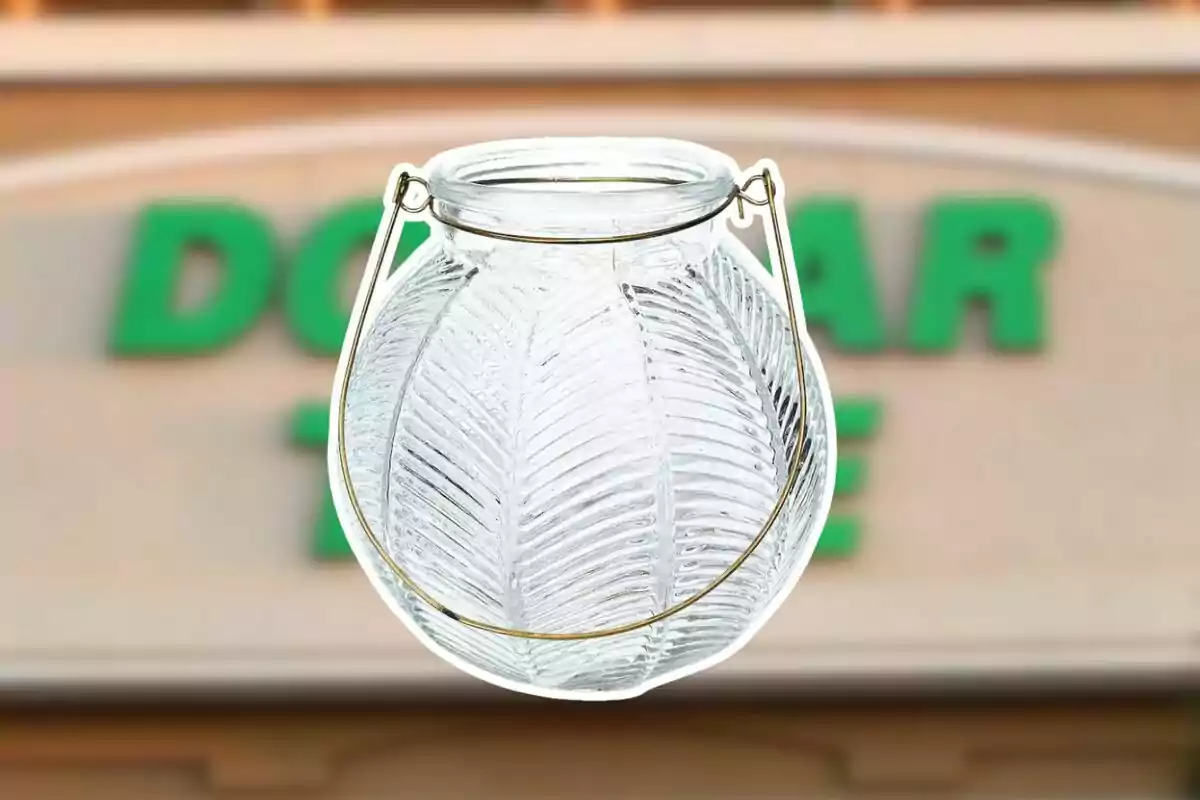 A clear glass jar with embossed leaves and a metal handle in front of a blurry store sign. A clear glass jar with embossed leaves and a metal handle in front of a blurry store sign.