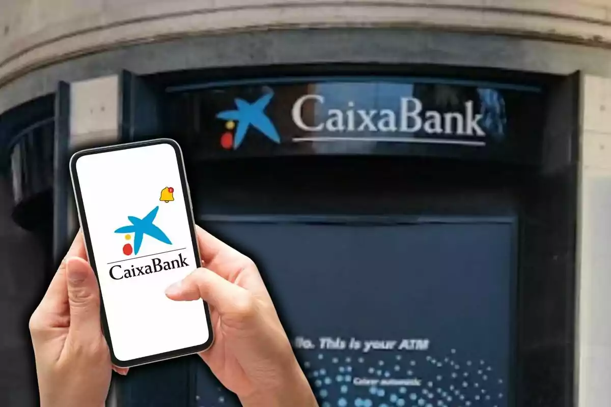 A person holds a mobile phone displaying the CaixaBank logo in front of a branch of the bank.