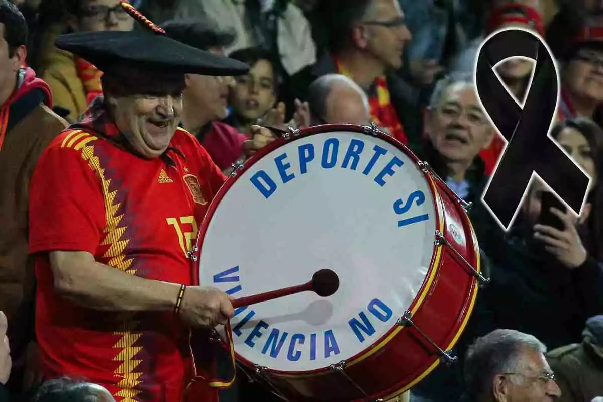 Manolo El del Bombo con camiseta roja y sombrero negro toca un tambor que dice "Deporte sí, Valencia no" mientras un lazo negro aparece al lado.