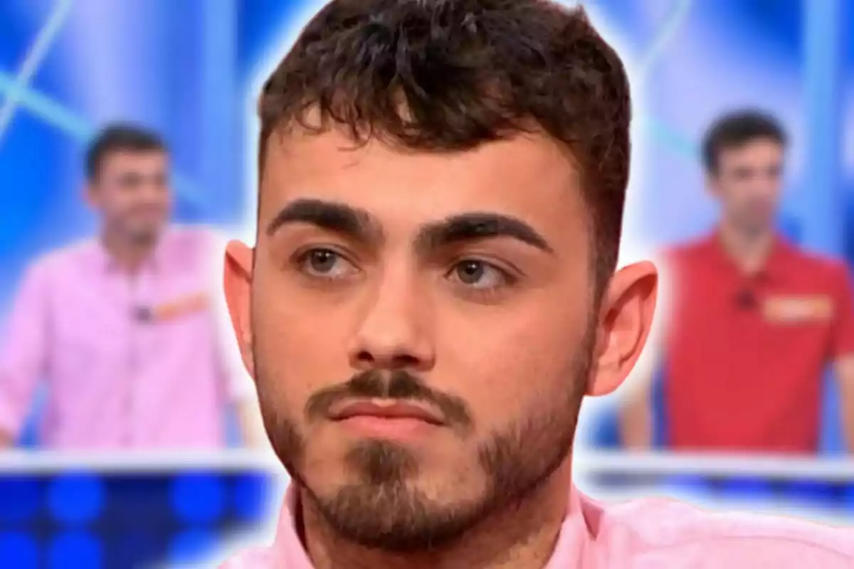 Raúl Santamaría con barba y cabello oscuro en primer plano con un fondo borroso de los Mozos de Arousa en un estudio de televisión.