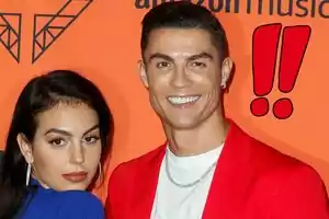 Georgina Rodríguez and Cristiano Ronaldo pose together in front of an orange background with a geometric design and the text 