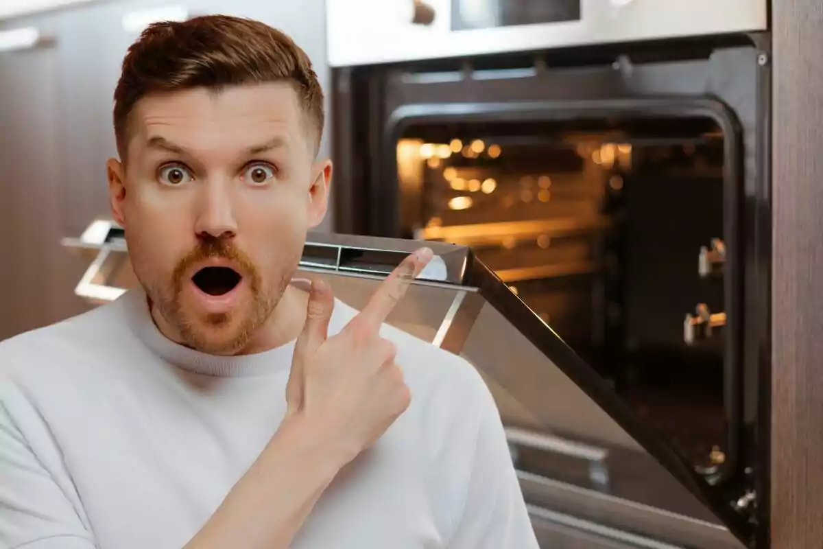 Hombre sorprendido señalando un horno abierto en una cocina moderna.