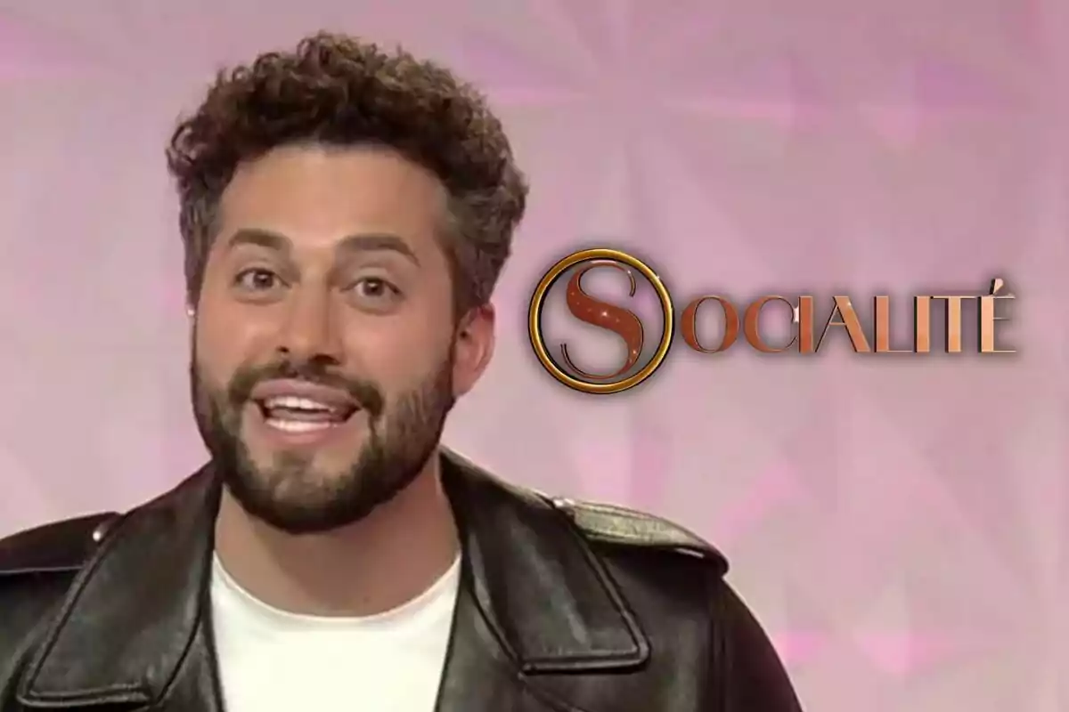 Javier de Hoyos con barba y chaqueta de cuero sonríe frente a un fondo rosa con el logo de "Socialité" a su lado.