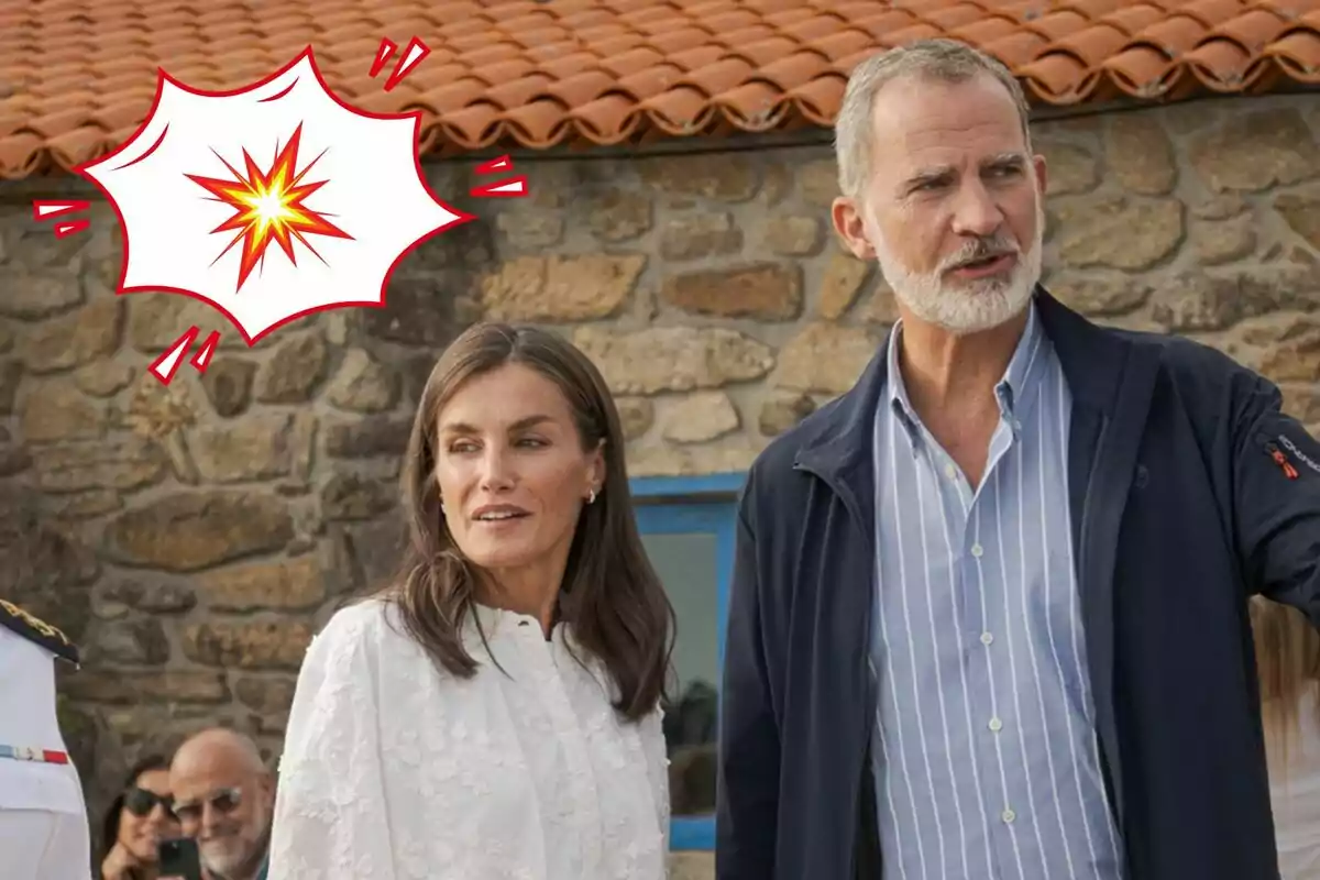 Letizia y Felipe VI de pie al aire libre frente a una pared de piedra con un techo de tejas rojas y un gráfico de explosión en la esquina superior izquierda.