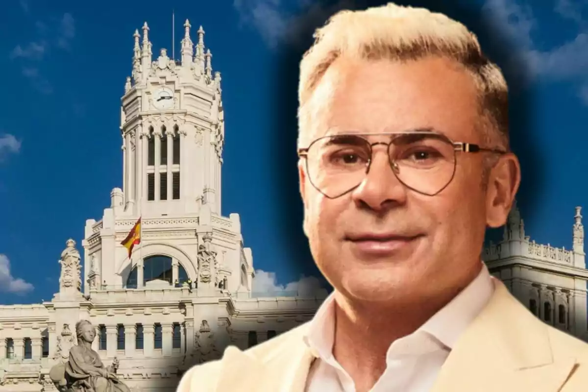 Jorge Javier Vázquez con chaqueta clara frente a un edificio histórico blanco con una bandera de España y cielo azul de fondo