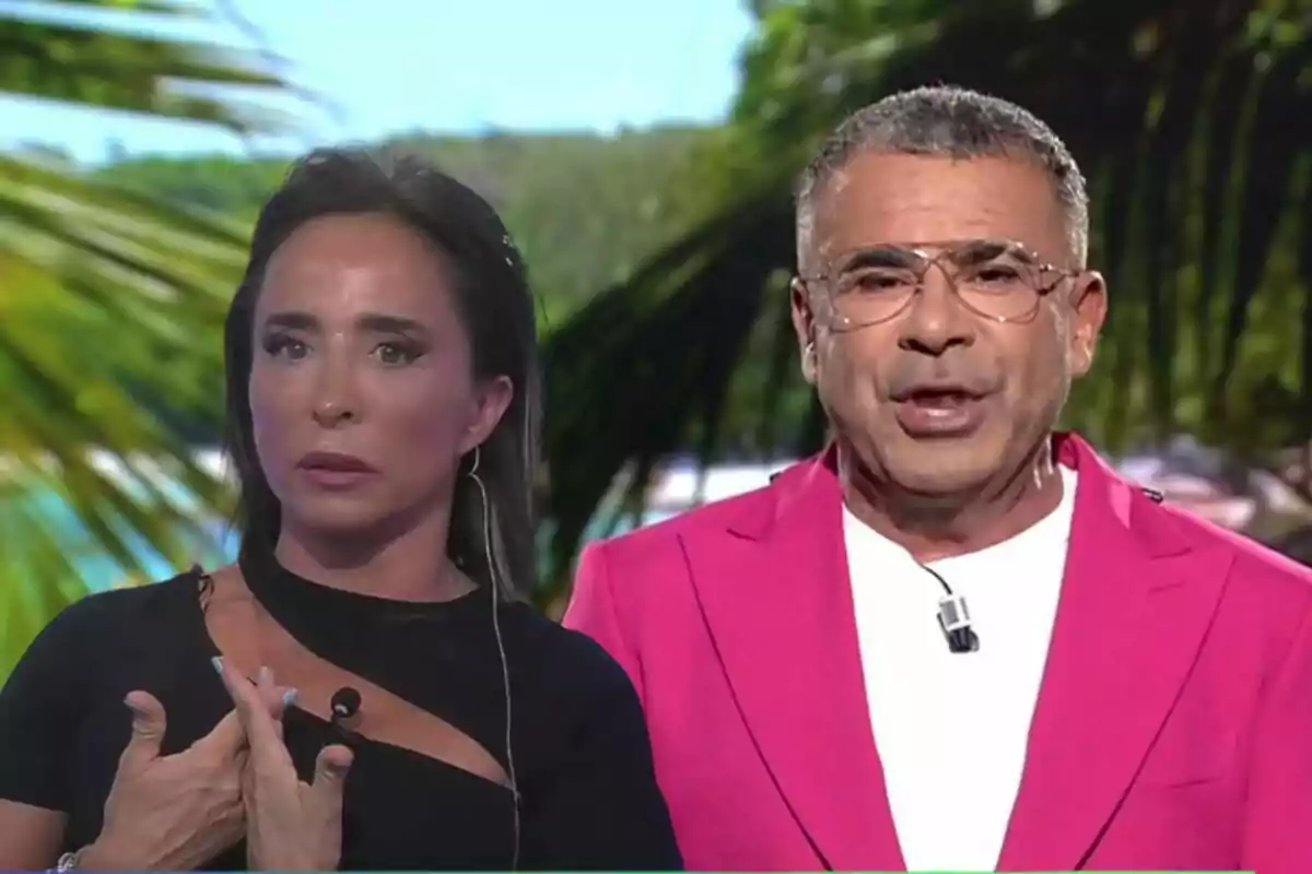 María Patiño y Jorge Javier Vázquez en 'Supervivientes' con un fondo de palmeras, María con vestido negro y Jorge Javier con chaqueta rosa.