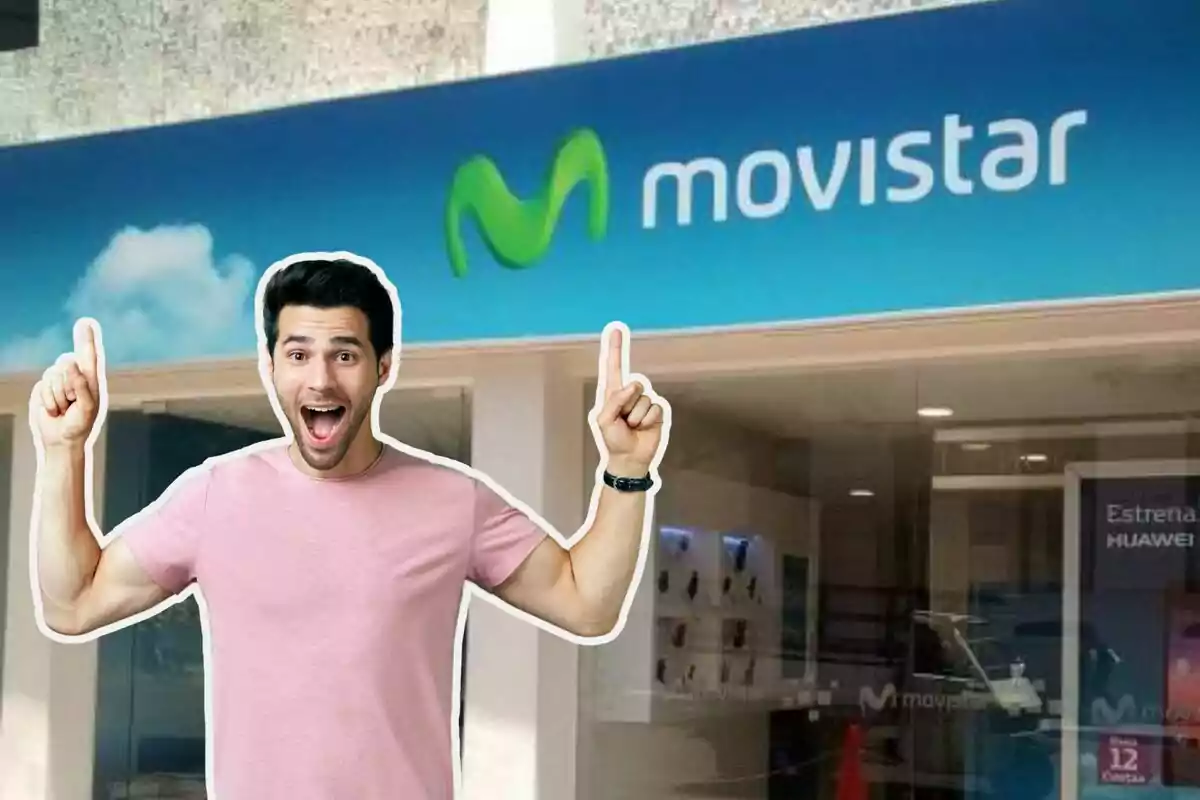 Un hombre con camiseta rosa y expresión de sorpresa señala hacia arriba con ambos dedos frente a una tienda de Movistar.