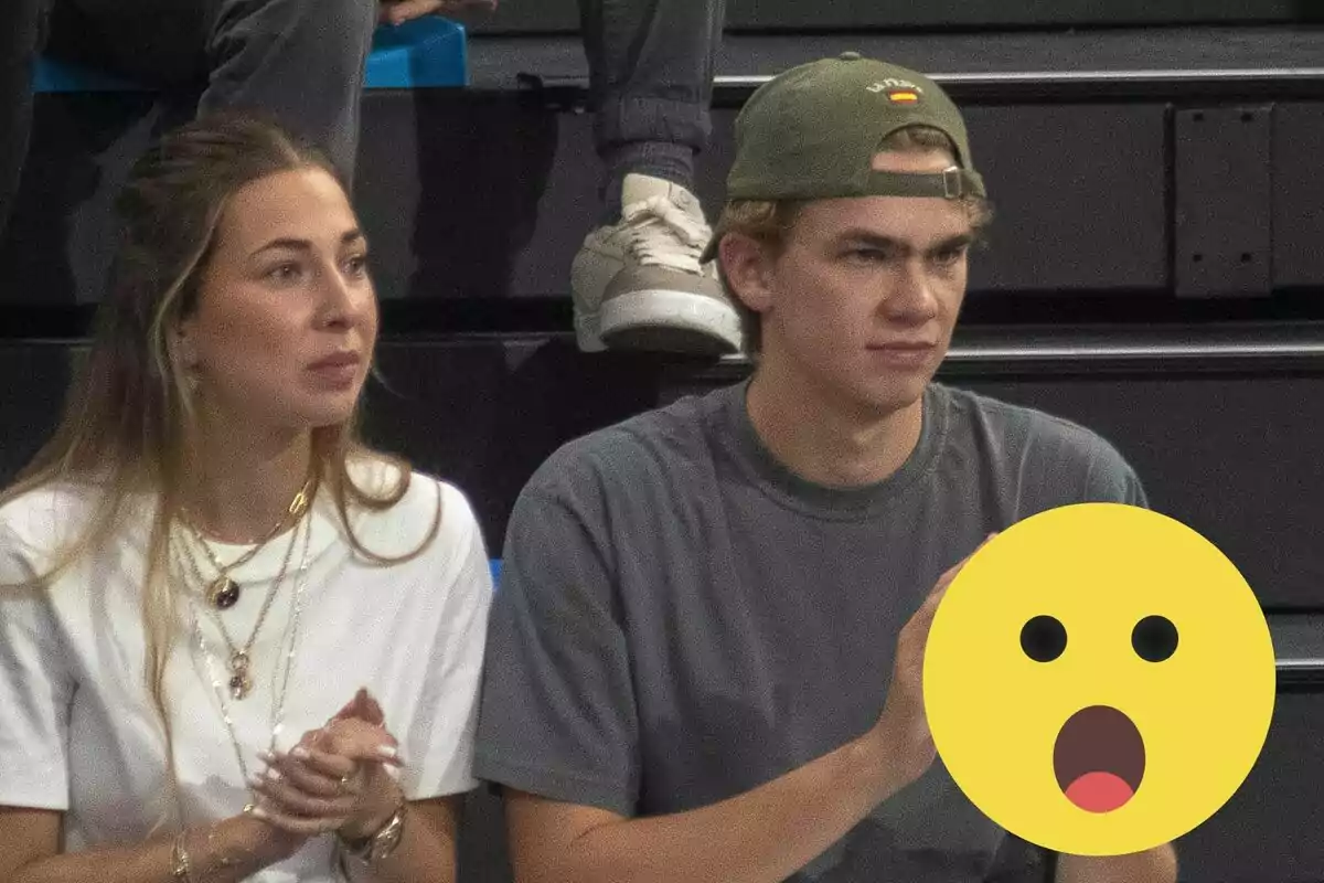 Olympia Beracasa y Miguel Urdangarin sentadas en unas gradas, una mujer con camiseta blanca y un hombre con gorra verde y camiseta gris, ambos parecen estar observando algo con atención.