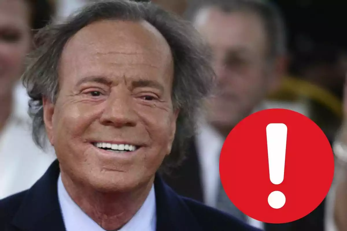 Julio Iglesias sonriente con un ícono de exclamación rojo en la esquina inferior derecha.