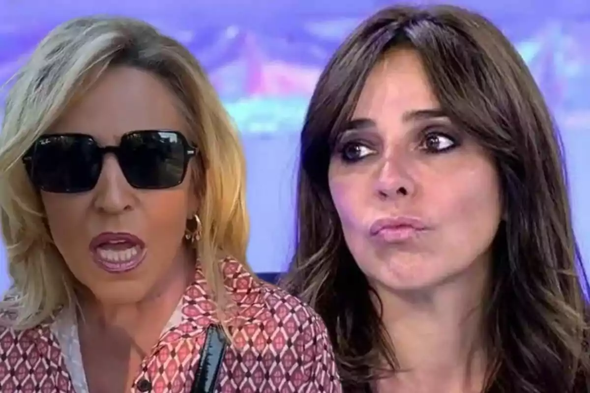 Lydia Lozano y Carmen Alcayde en primer plano, una con gafas de sol y cabello rubio, la otra con cabello castaño y expresión seria, sobre un fondo azul difuminado.