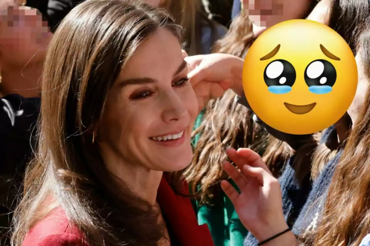 La reina Letizia sonriente rodeada de otras personas con un emoji cubriendo el rostro de una de ellas.