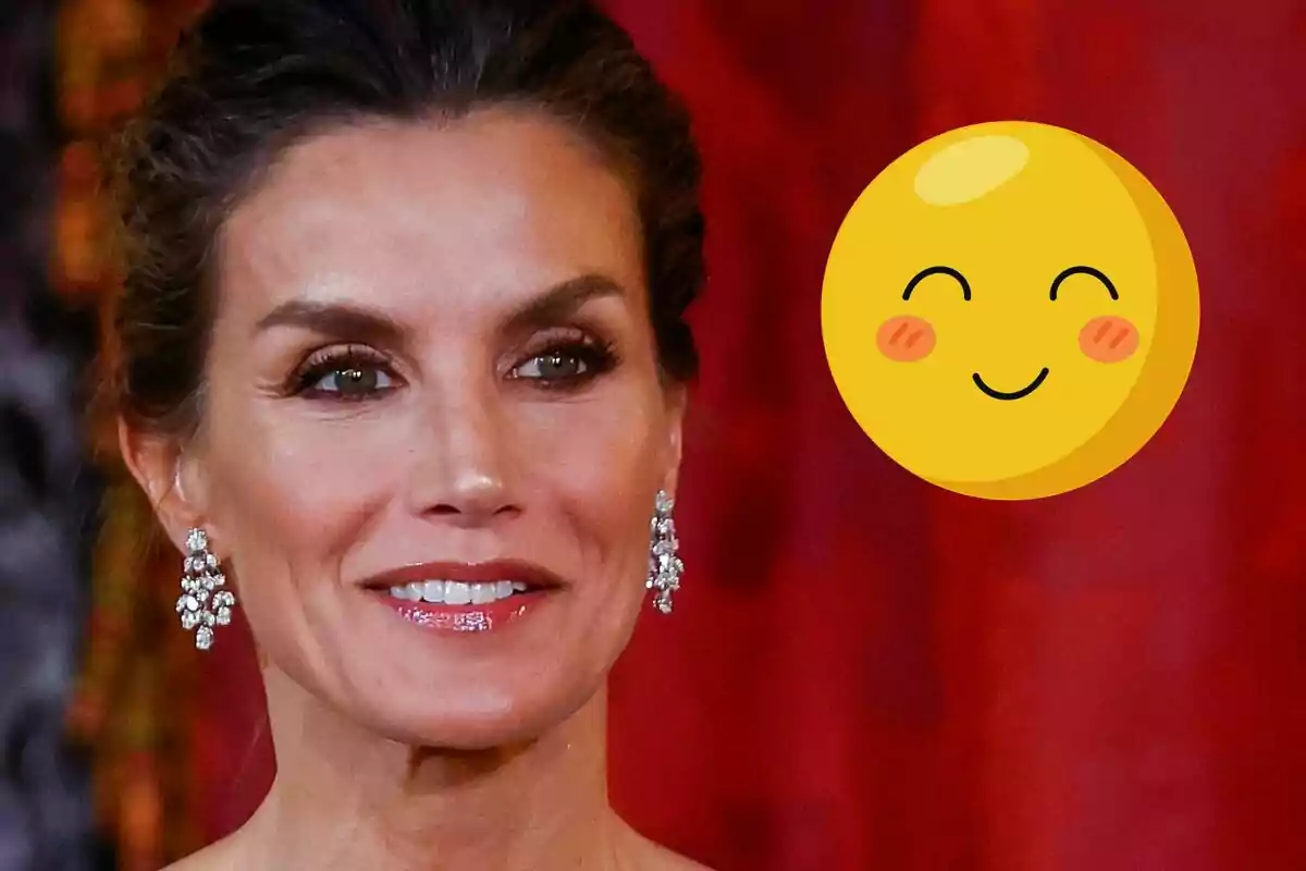 Queen Letizia with sparkling earrings smiles in front of a red background, accompanied by a smiling emoji.