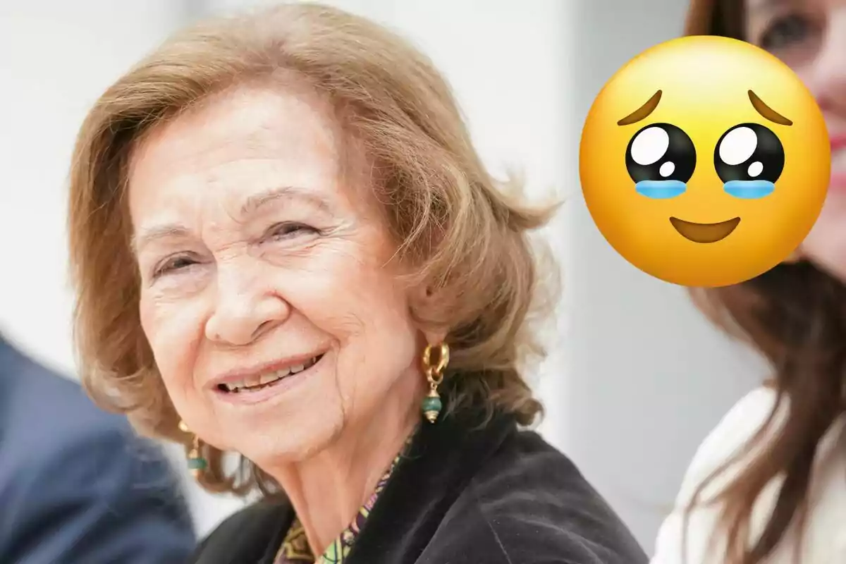 La reina Sofía sonríe mientras un emoji con ojos llorosos está superpuesto a la imagen.