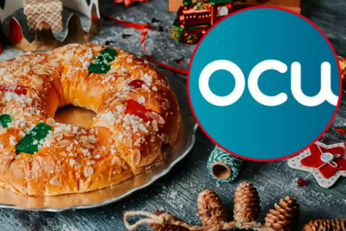 Un roscón de Reyes decorado con frutas confitadas y almendras junto a un logotipo de la OCU en un ambiente festivo.