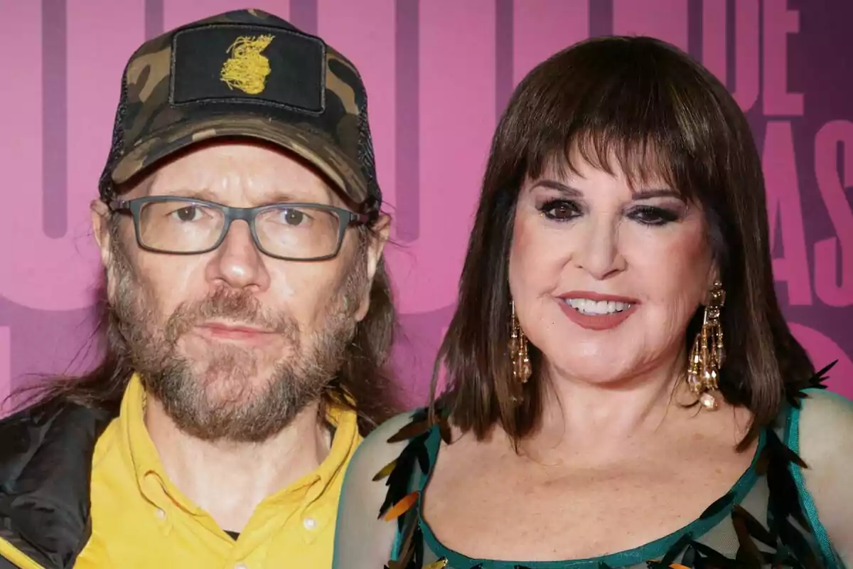 Una pareja posando frente a un fondo rosa en un evento, el hombre lleva una gorra de camuflaje y gafas, mientras que la mujer luce un vestido verde y pendientes dorados.