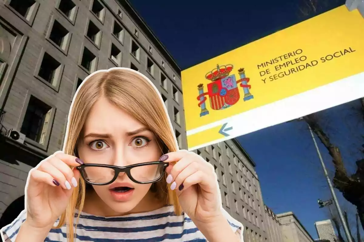 Una mujer con expresión de sorpresa sostiene sus gafas frente a un edificio con un cartel del Ministerio de Empleo y Seguridad Social de España.